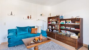 A living room with a teal sofa, a coffee table with decorative items, a bookshelf filled with books, and a floor lamp. - Holiday Apartment 'Ludwigsburg' with Wi-Fi (Ludwigsburg)