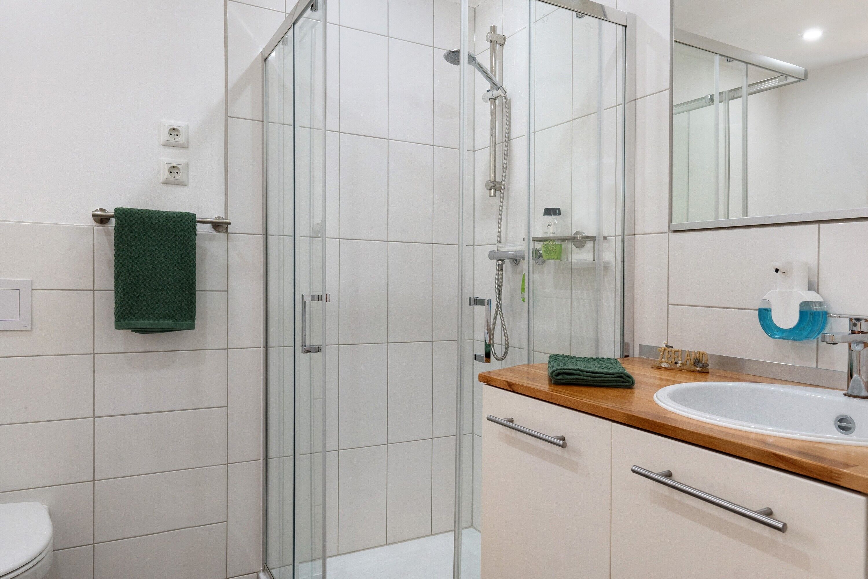 A modern bathroom with a glass shower enclosure, a wooden vanity with a sink, and a mirror above the vanity.