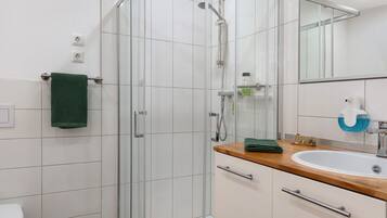 A modern bathroom with a glass shower enclosure, a wooden vanity with a sink, and a mirror above the vanity.