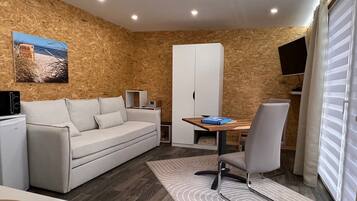 A modern room with a sofa, a dining table, a chair, a TV, and a window with blinds.