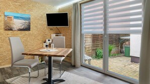 Una habitación moderna con una mesa de madera, dos sillas, un televisor de pantalla plana y un amplio ventanal corredero a un patio.