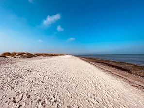 Een zandstrand met voetafdrukken die naar het water leiden, een heldere lucht en een verre horizon.