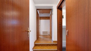 Un couloir avec des portes en bois, un parquet en point de Hongrie et, au fond, une petite armoire blanche.