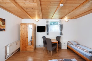Una habitación con techo de madera, una cama, un escritorio con sillas, un televisor y una ventana con cortinas.