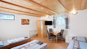 Une pièce avec un plafond en bois, un lit avec une literie à motifs, un bureau avec une chaise, une télévision et une fenêtre avec des rideaux.