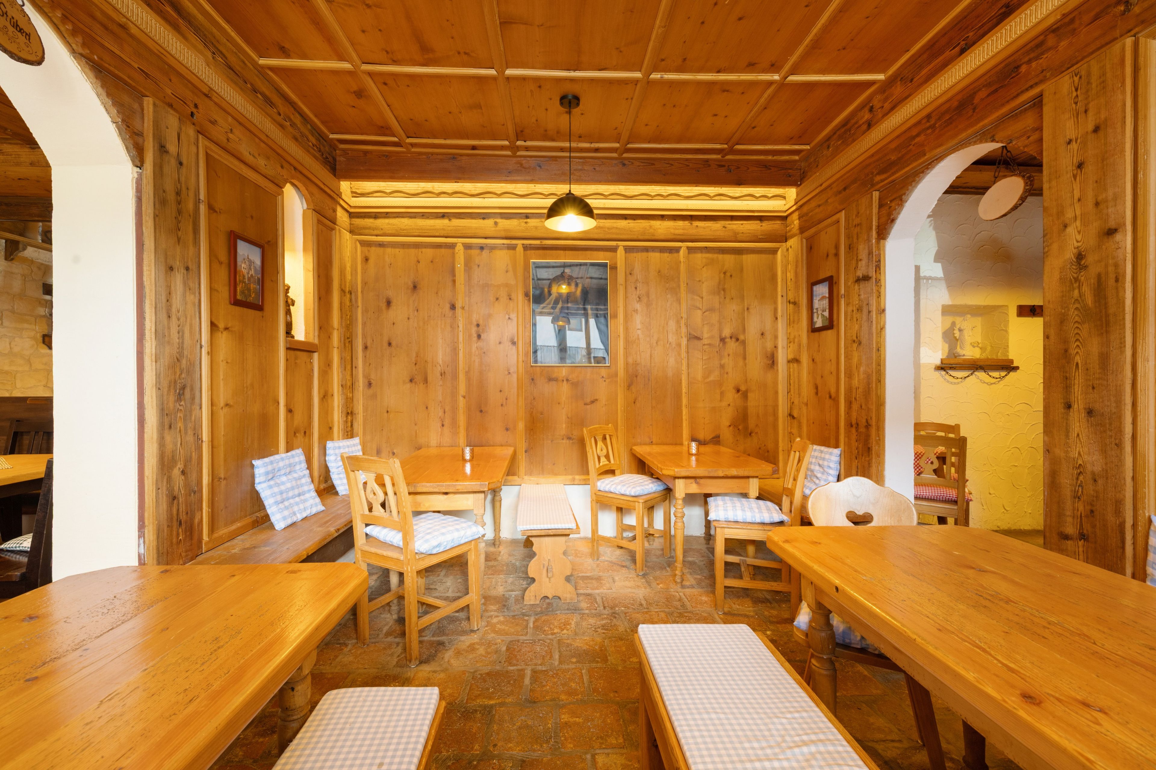 Un intérieur en bois, avec un sol en pierre, des tables et des chaises en bois, et un luminaire suspendu.