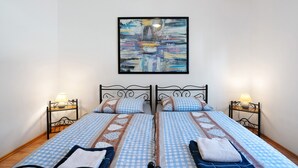 Un lit double avec une literie à carreaux, deux tables de chevet avec des lampes et un tableau abstrait encadré au-dessus du lit.