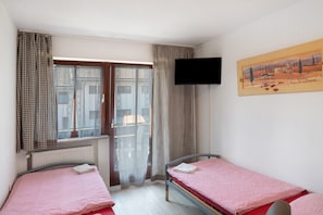 A bedroom with two single beds, a window with curtains, a radiator, and a television on the wall.