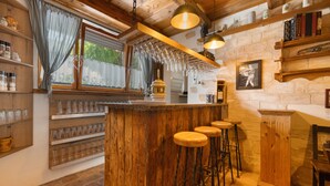 A rustic bar area with wooden bar stools, a wine rack, and a stone wall. - Knödelhof 'Room 4', 3-Bed Room – Guesthouse near Munich (Putzbrunn)