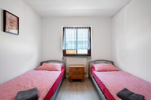 A small, clean room with two single beds, a wooden nightstand, a window with lace curtains, and a framed picture on the wall. - Knödelhof ‘Room 4’, 3-bed room with shared terrace and WLAN (Putzbrunn)