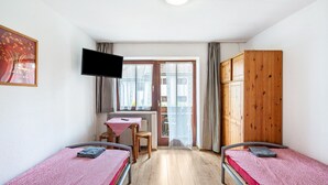 Ein Zimmer mit zwei Einzelbetten, einem Schreibtisch, einem Stuhl, einem Fernseher und einem Fenster mit Vorhängen.