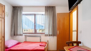 Een kleine kamer met een bed, een tafel, een stoel, een televisie en een raam met gordijnen.