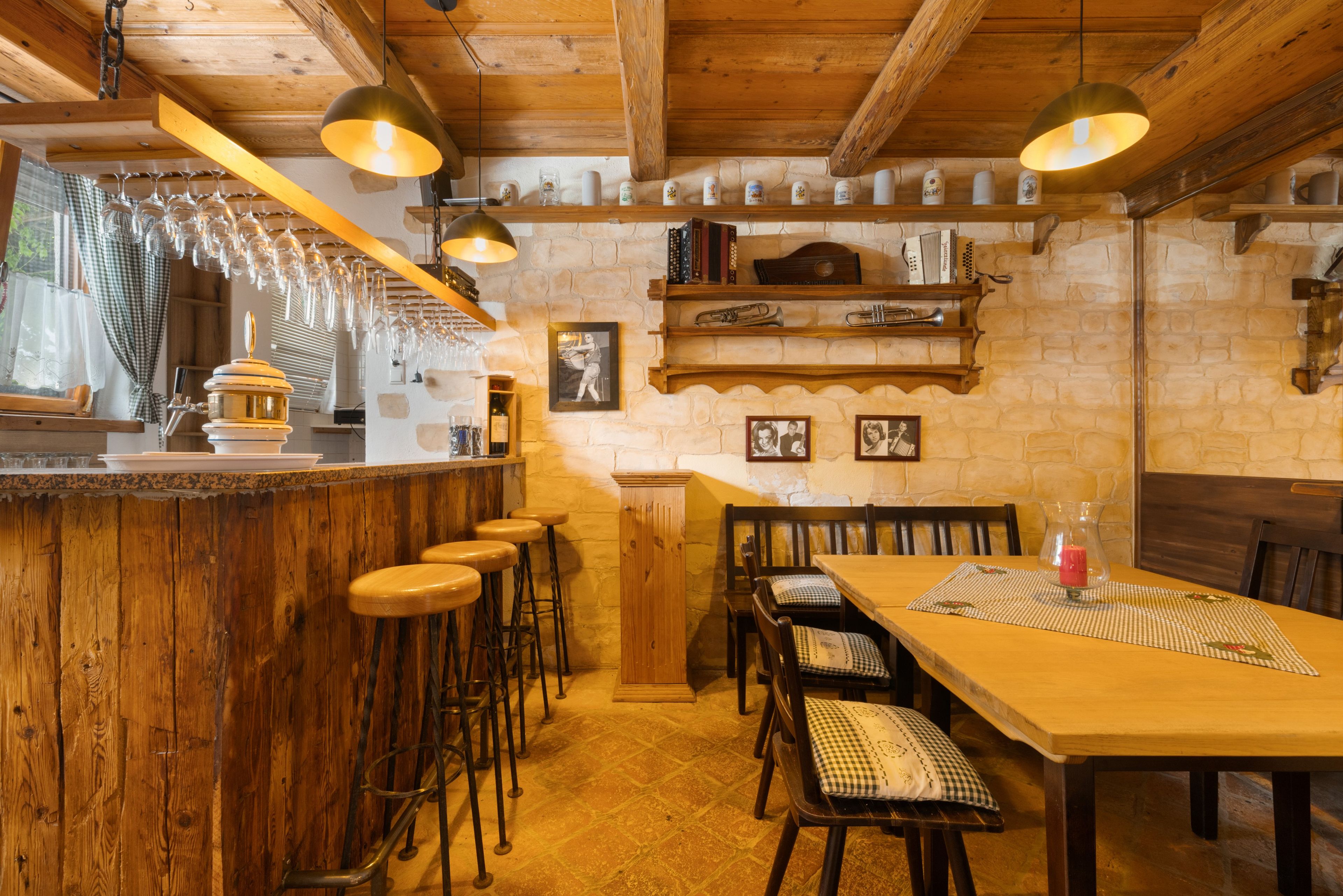 Ein rustikales Interieur mit Barbereich, Holzhockern, einem Esstisch mit Stühlen und einer Steinwand.