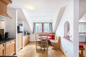 Une cuisine avec des meubles de rangement en bois, une table à manger avec des chaises et une fenêtre avec des rideaux.