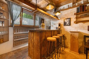 A rustic bar area with wooden bar stools, a wine rack, and a stone wall. - Knödelhof 'Room A', Twin Room – Guesthouse near Munich (Putzbrunn)