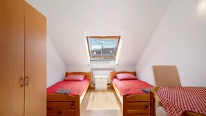 Une petite chambre avec deux lits en bois, une fenêtre, un radiateur et une armoire.
