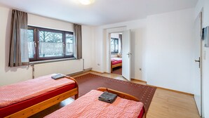 A room with two single beds, a radiator, a window with curtains, and a door leading to another room. - Knödelhof 'Apartment 8' – Guesthouse near Munich & Trade Fair (Putzbrunn)