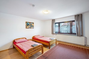 Une pièce avec deux lits en bois, une fenêtre avec des rideaux, un radiateur et un tableau accroché au mur.
