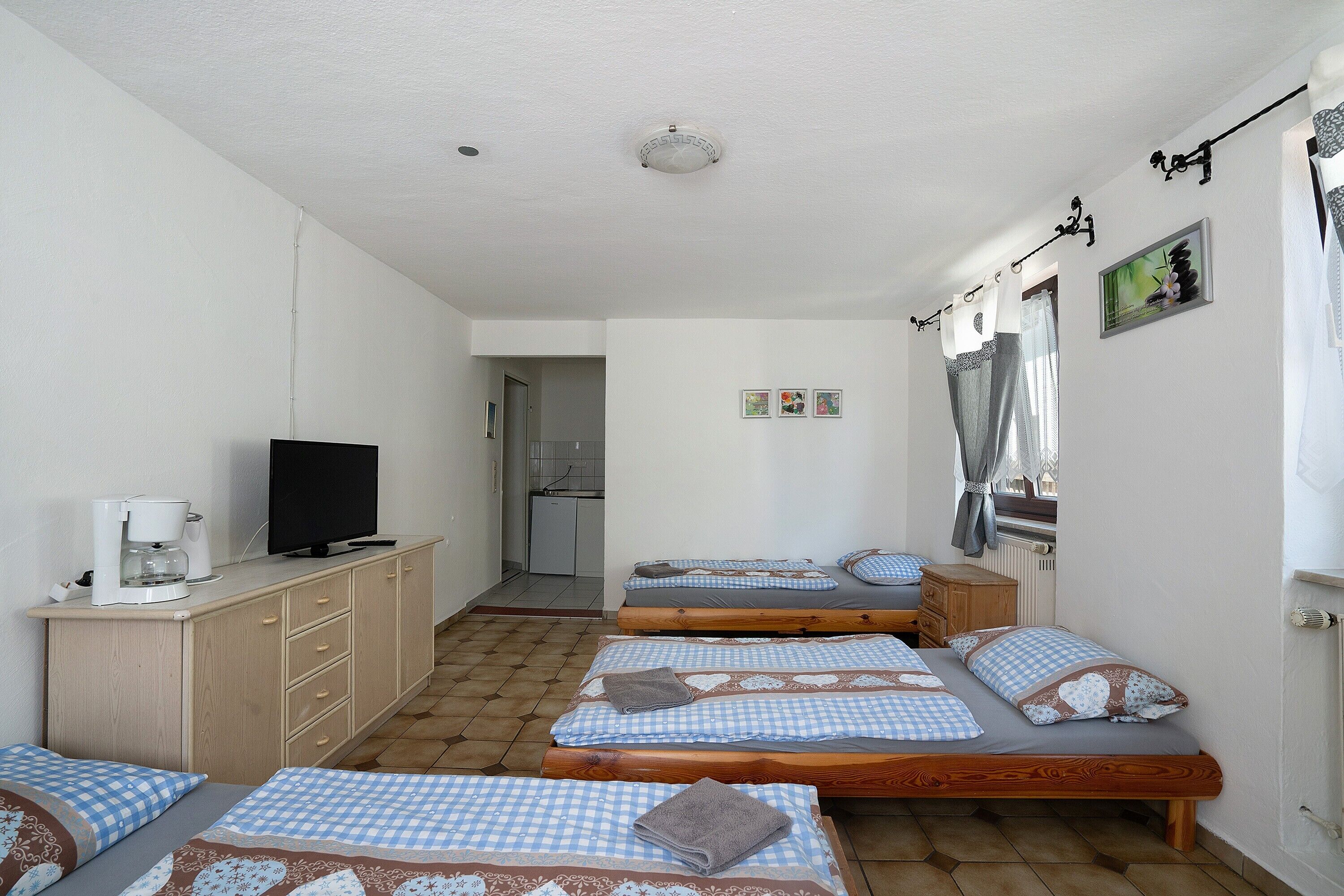 A room with three beds, a television, a coffee maker, and a small kitchen area.