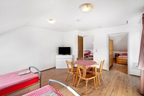 A compact room with a bed, a desk, a chair, a television, and a small table with a checkered tablecloth.