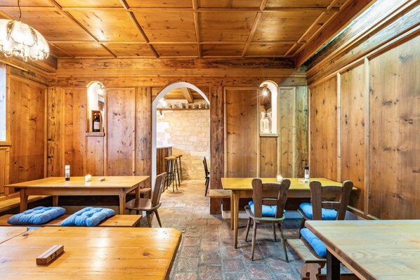 A wooden interior with tables and benches, stone walls, and arched doorways.