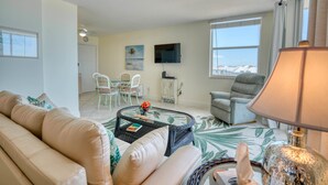 A living room with a sofa, a coffee table, a TV, and a chair. There is a window with a view of the sea. - Surreal Gulf Views Close To The Beach 3606 (Bonita Springs)