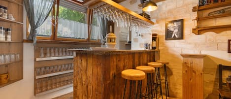 A rustic bar area with wooden bar stools, a wine rack, and a stone wall.