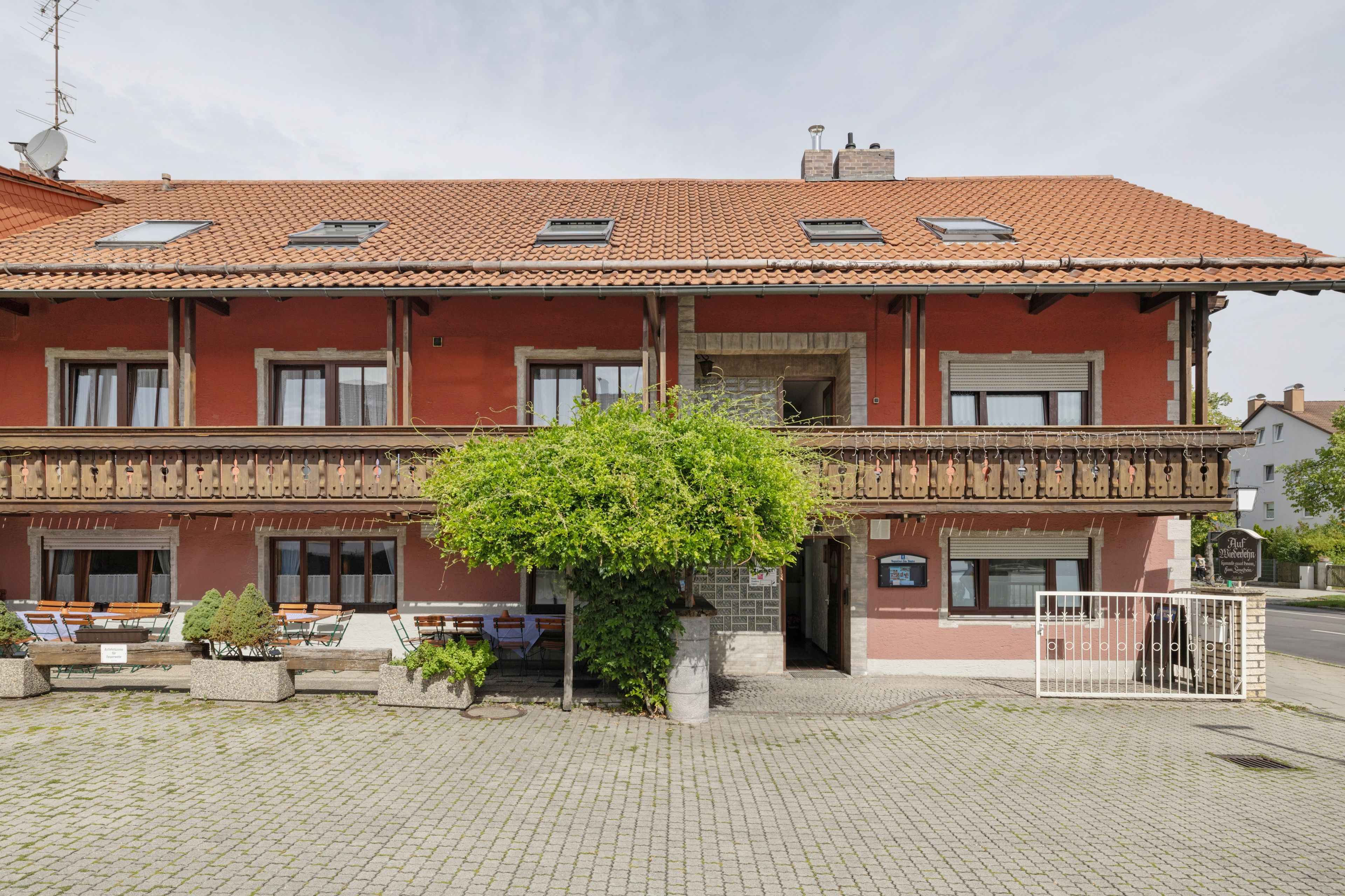 A two-story building with a red facade, multiple windows, and a small tree in the foreground.