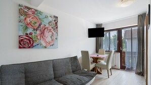 Ein modernes Wohnzimmer mit grauem Sofa, einem Esstisch mit Stühlen, einem Flachbildfernseher und einem großen floralen Wandbild.