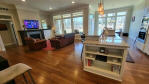 A spacious living area with a fireplace, a large window, and a kitchen island. - Cuthbert Place | Single-Level, 1.5mi Mayo, Pets OK (Rochester)