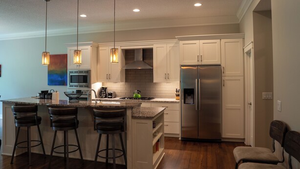 A modern kitchen with white cabinets, a stainless steel refrigerator, and a central island with bar stools. - Cuthbert Place | Single-Level, 1.5mi Mayo, Pets OK (Rochester)