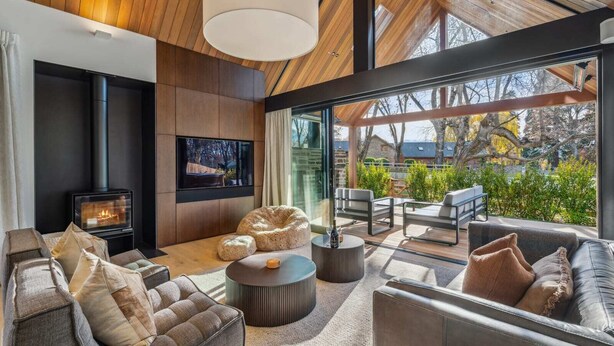 A modern living room with a fireplace, comfortable seating, and large windows offering a view of the outdoors. - MacAndrew Luxury Lodge (Wānaka)