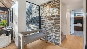 A modern room with a stone wall, a bench, a bed, and a view of the outdoors. - MacAndrew Luxury Lodge (Wānaka)