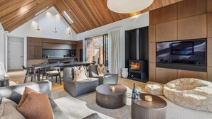A modern living room with a high ceiling, a fireplace, and a flat-screen TV mounted on the wall. - MacAndrew Luxury Lodge (Wānaka)
