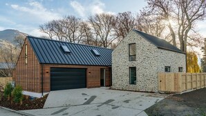 A modern two-story house with a garage, stone exterior, and a metal roof. - MacAndrew Luxury Lodge (Wānaka)