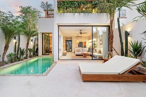 A modern outdoor living area with a pool, lounge chairs, and a glass-enclosed interior space with a sofa and coffee table. - Villa Lago (Pecatu)