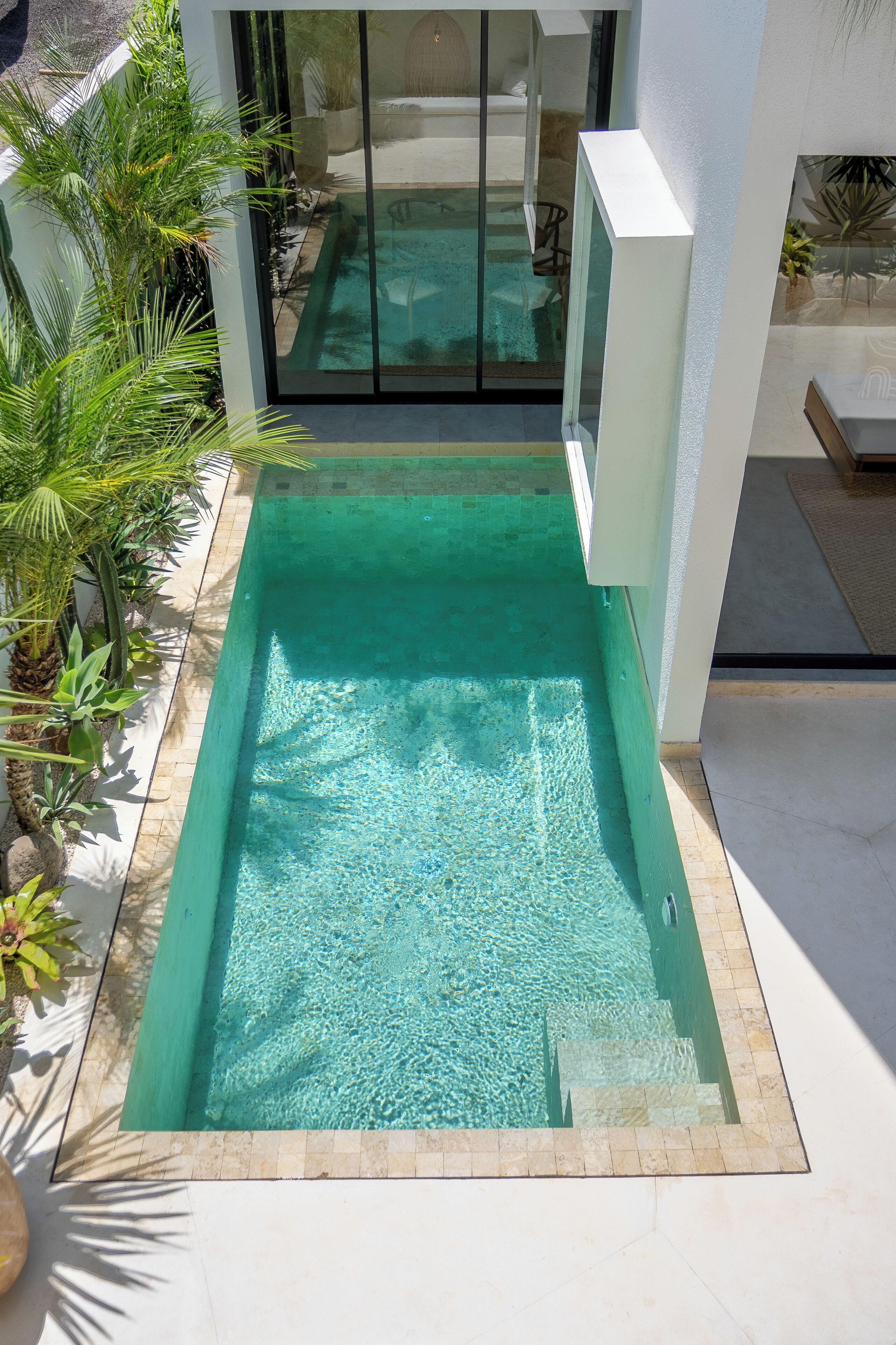 A rectangular swimming pool with clear water, surrounded by a tiled deck and potted plants.