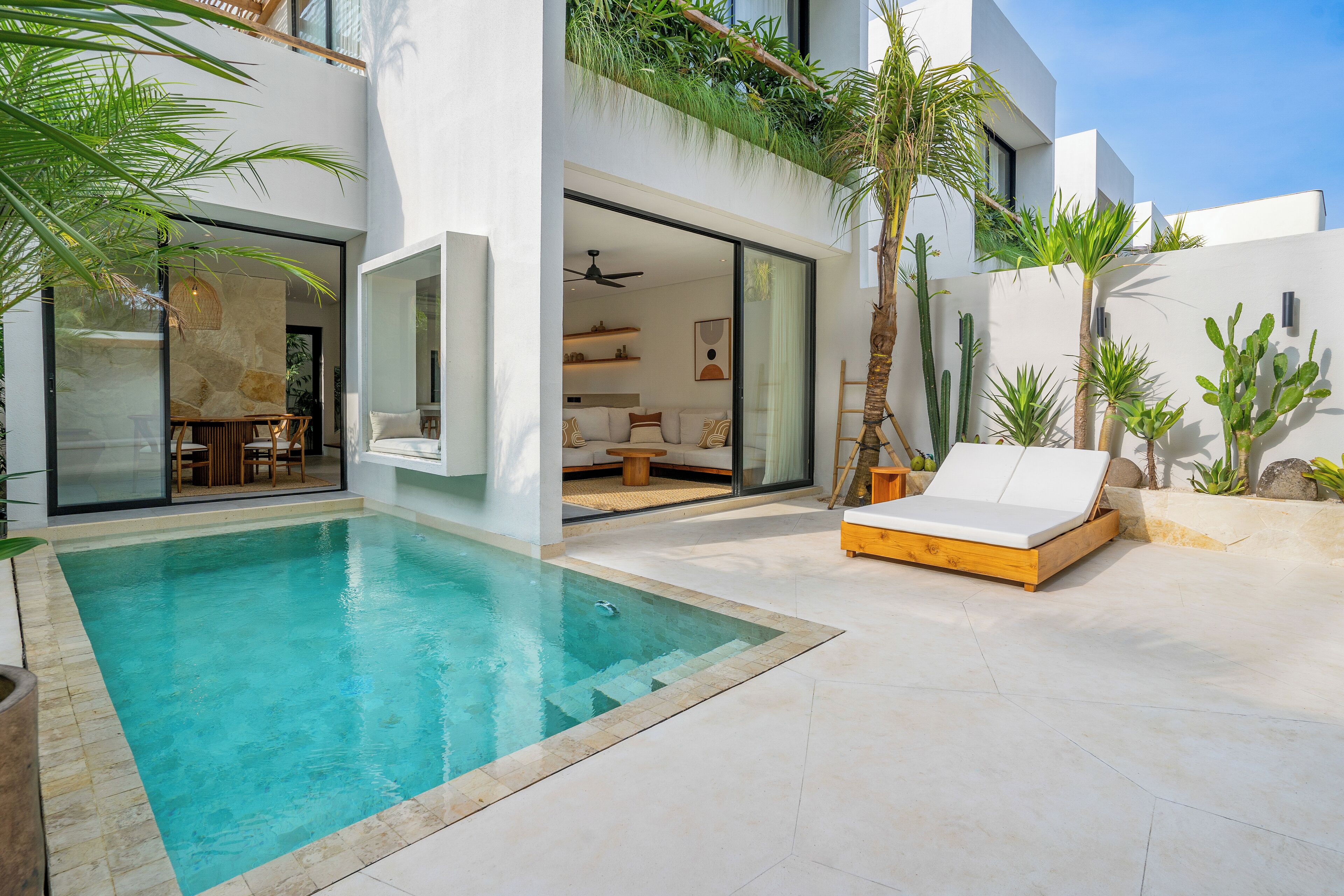 A modern house with a swimming pool, a sun lounger, and a patio area with plants.