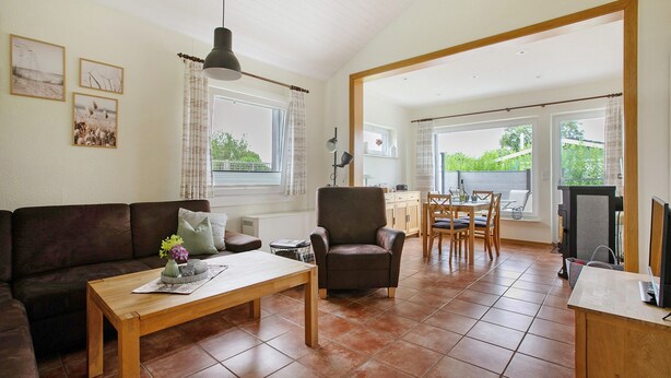 A living room with a sofa, a wooden coffee table, a brown armchair, a dining area with a table and chairs, and a TV on a stand. - Apartment 'Drybarg' with Private Terrace, Private Garden and Wi-Fi (Simonsberg)