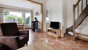 A living room with a sofa, TV stand, and staircase. - Apartment 'Drybarg' with Private Terrace, Private Garden and Wi-Fi (Simonsberg)
