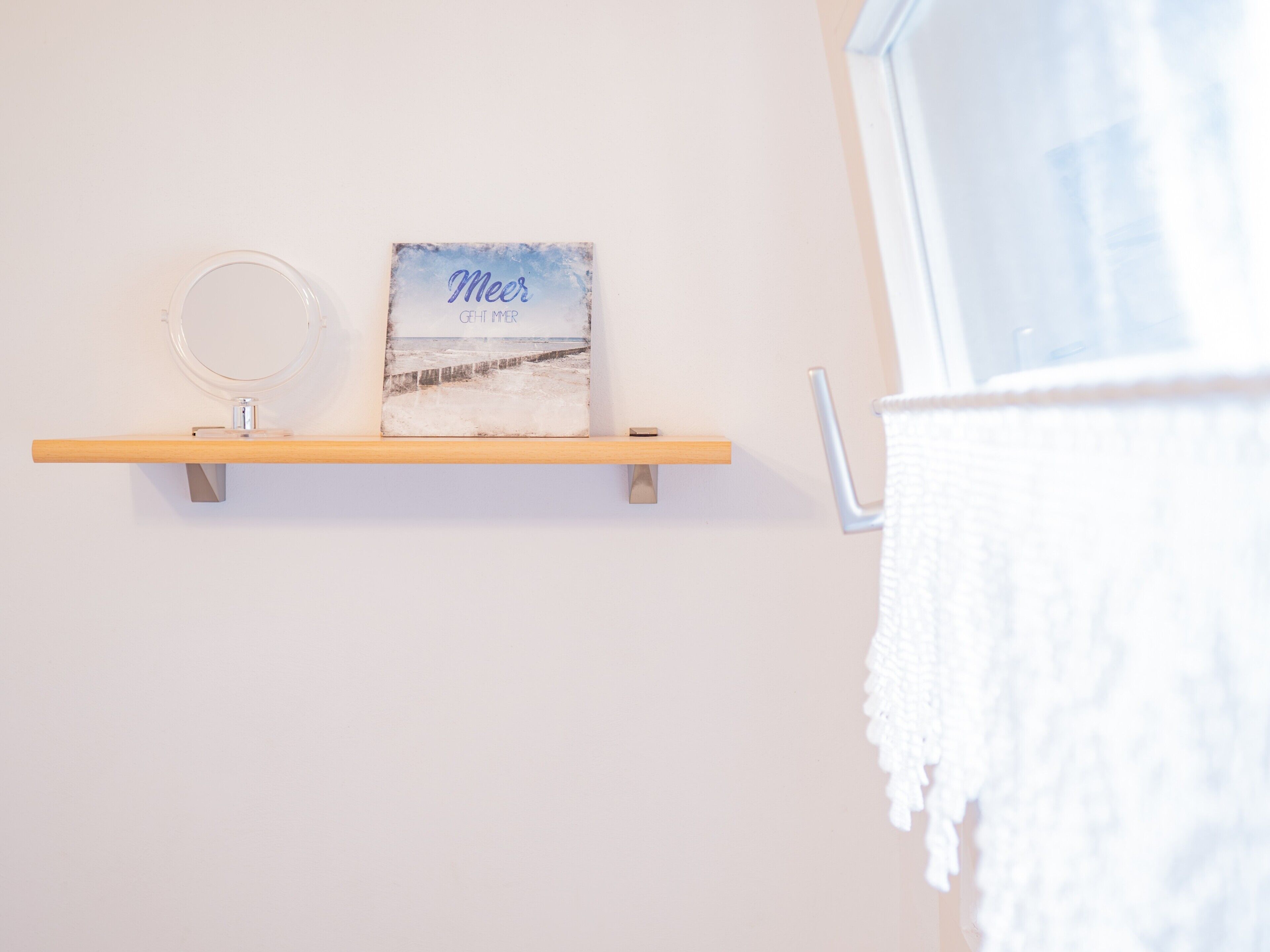 Une salle de bain avec une étagère en bois sur laquelle sont posés un tableau encadré et un miroir rond.