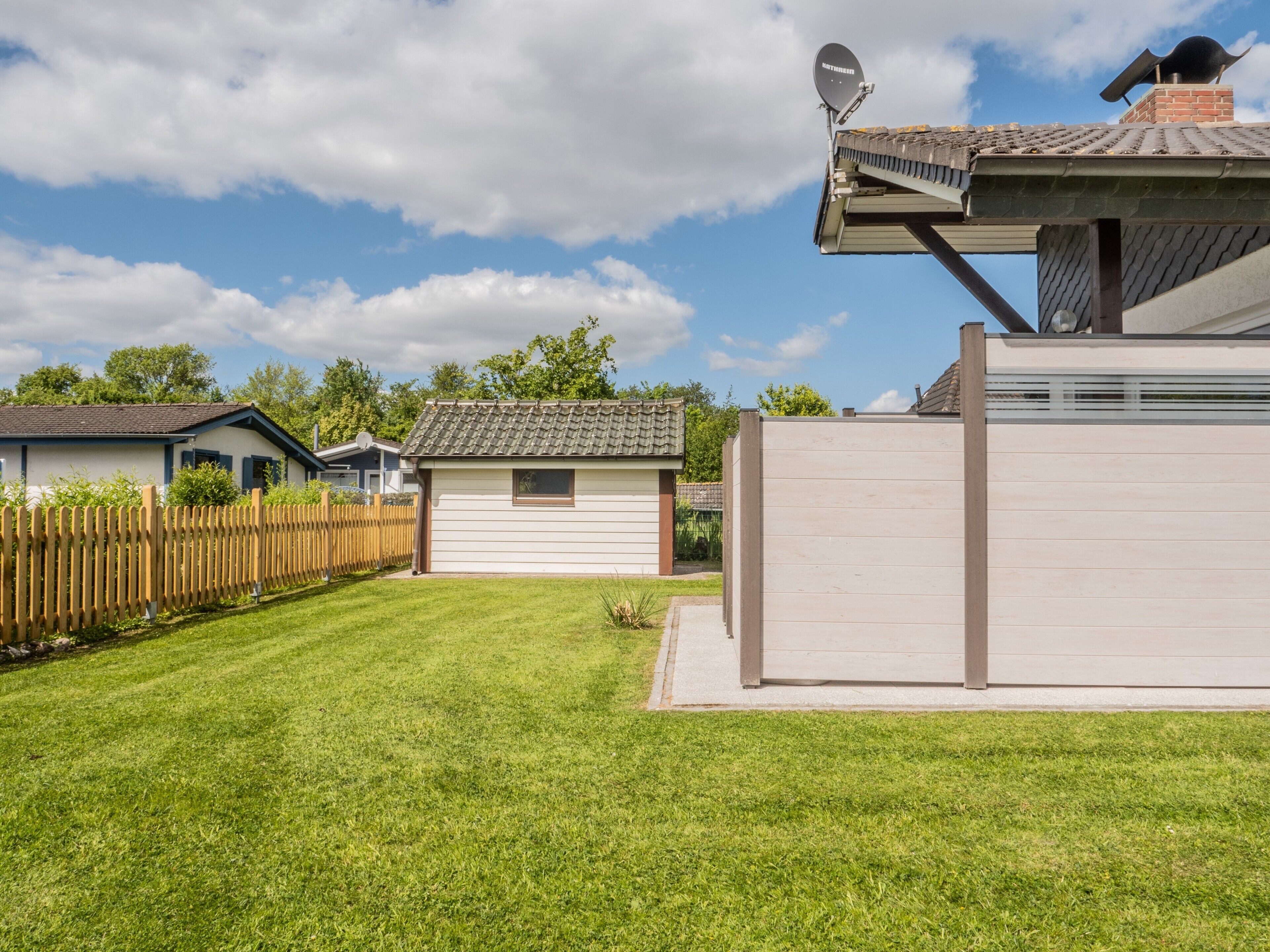 Un quartier résidentiel avec une pelouse bien entretenue, une clôture en bois et des maisons équipées d’antennes paraboliques.