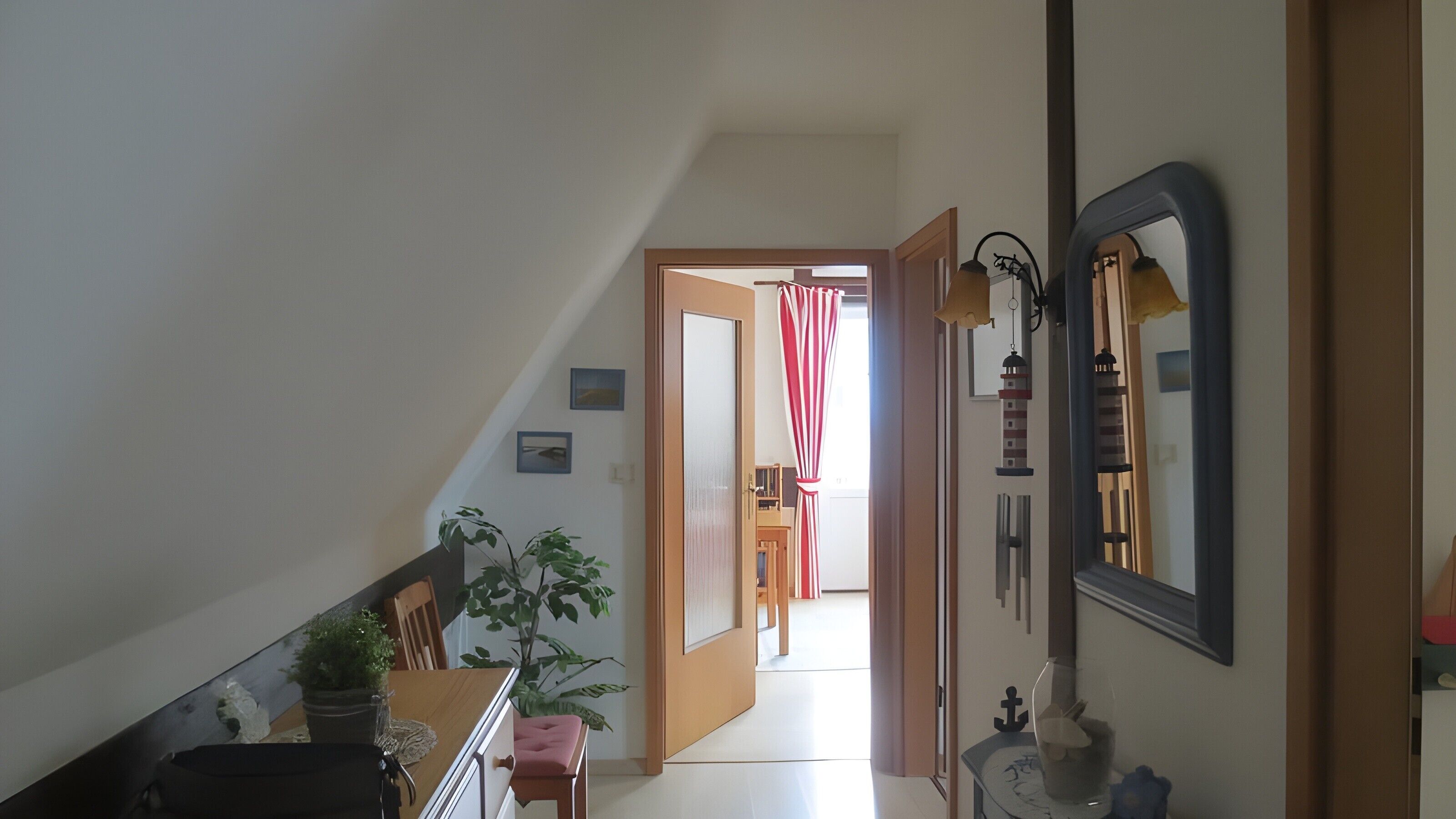 A hallway with a staircase, a door leading to another room, a potted plant, and a mirror on the wall.