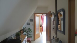 A hallway with a staircase, a door leading to another room, a potted plant, and a mirror on the wall.