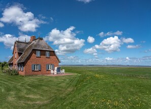 A red brick house with a thatched roof, a lawn, and a view of the sea. - Holiday Home 'Reethuus Am Fething' with Sea View, Private Garden and Wi-Fi (Langeneß)
