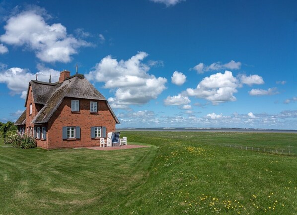A red brick house with a thatched roof, a lawn, and a view of the sea.