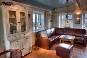 A cozy living room with a brown leather sofa, a wooden coffee table, a white cabinet with glass doors, and a window with curtains.