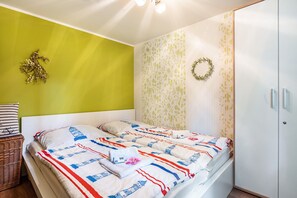 Une pièce comprenant un lit, un panier en osier, un mur orné d’un motif vert et blanc, et une armoire.