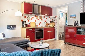 Une cuisine moderne avec des meubles rouges, un coin repas doté d’une table ronde et un salon avec un canapé.