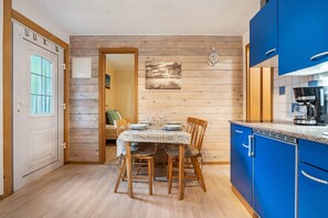 A compact kitchen with blue cabinets, a dining table set for four, and a wooden floor.